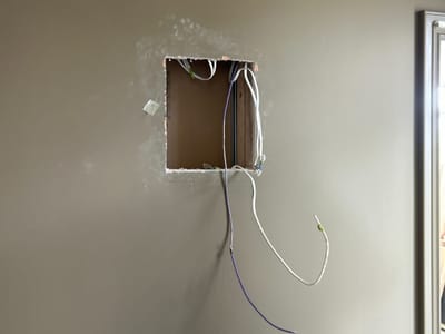 Opening cut in a plasterboard wall with a cable left loose and the edges not made good